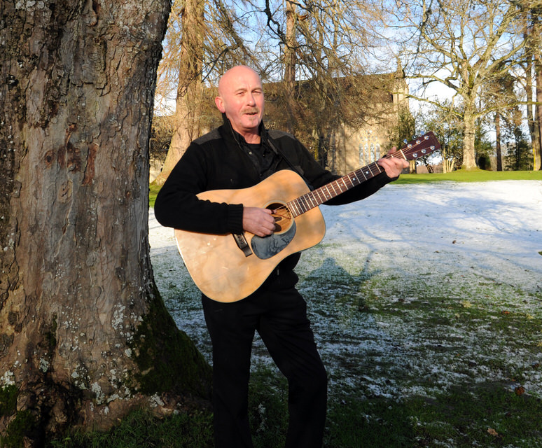 Fraser Nimmo plays guitar by an old church